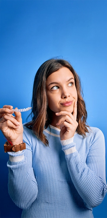 Girl In Sweater Holding Invisalign Aligner On Blue Background